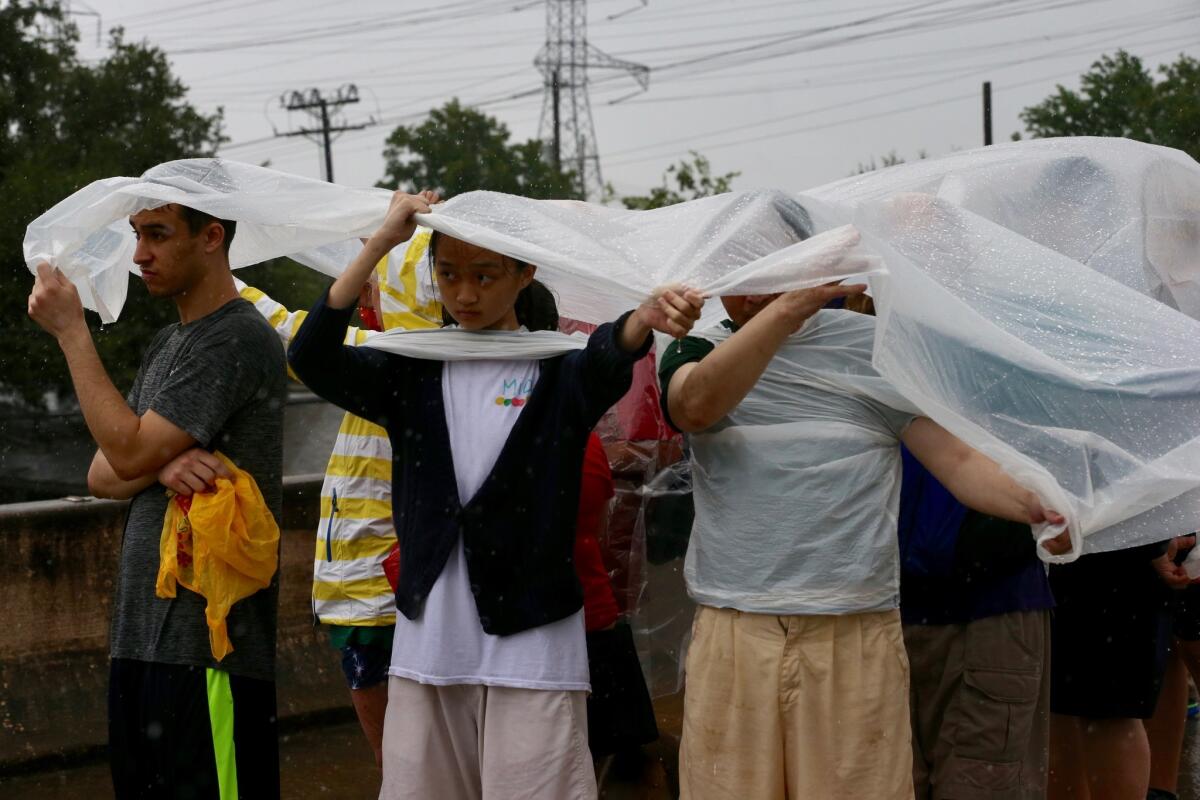 Evacuees huddle under a plastic sheet to guard from the rain as they wait for transportation to an evacuation center in Houston,.