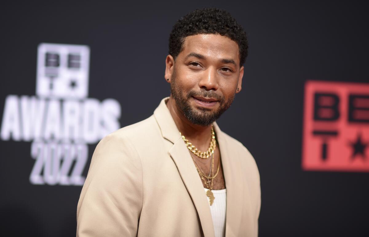 A man wearing a beige blazer and gold necklaces