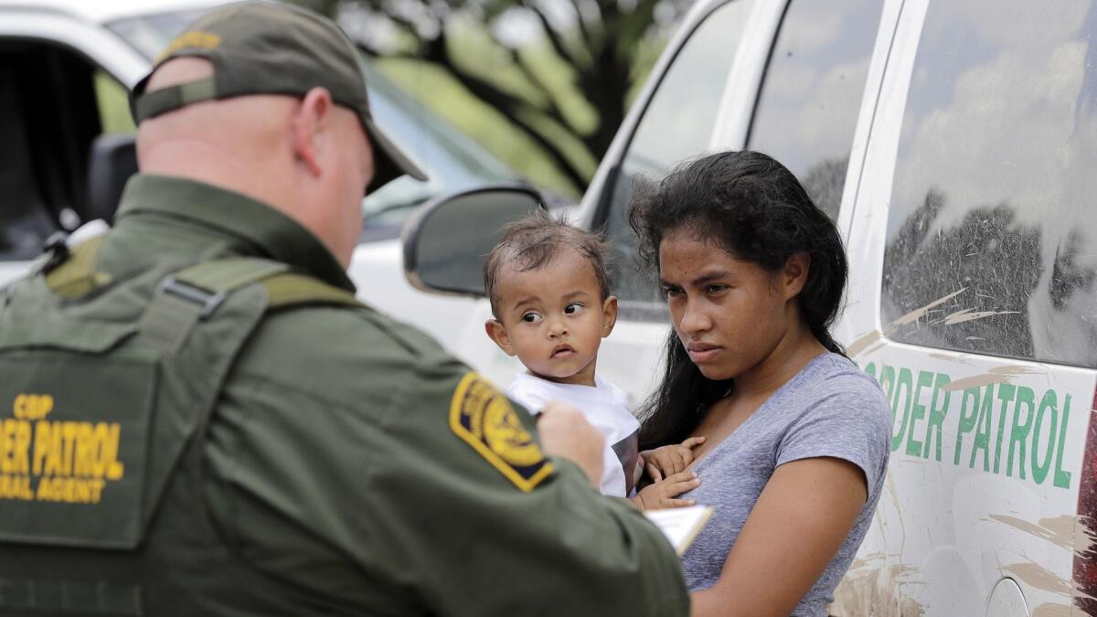 A mother migrating from Honduras holds her 1-year-old child while surrendering to U.S. Border Patrol agents on June 25 after authorities said she illegally crossed the border, near McAllen, Texas.