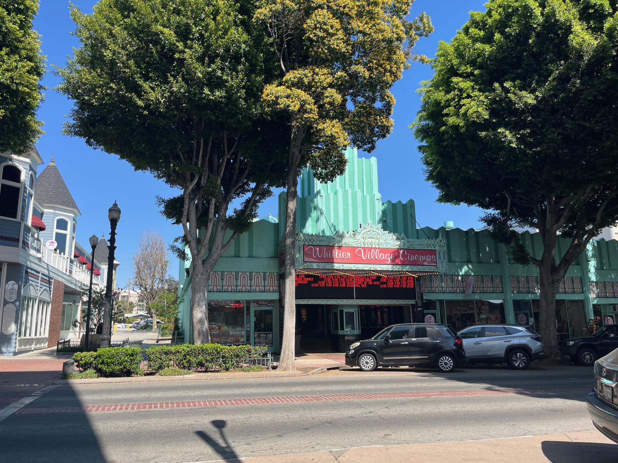 Tall trees flank the entrance of an art deco movie theater, the Whittier Village Cinema