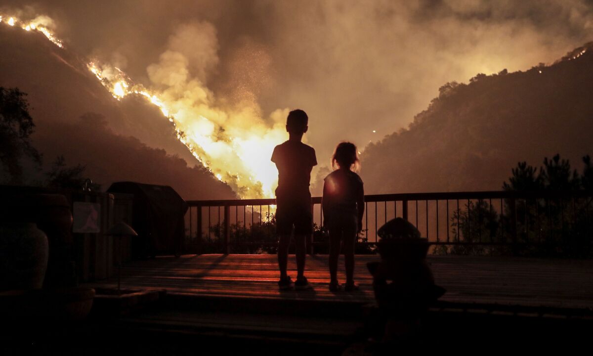 Children look on as flames engulf the hillsides behind their backyard in Monrovia as the 2020 Bobcat Fire burns nearby. 