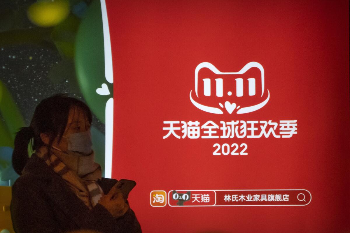 A woman waits for a bus at a bus stop next to an advertisement for Tmall's Singles' Day sale in Beijing, Wednesday, Nov. 9, 2022. China's biggest online shopping festival, known as Singles' Day, is typically an extravagant affair as Chinese e-commerce firms like Alibaba and JD.com ramp up marketing campaigns and engage top livestreamers to hawk everything from lipstick to furniture as they race to break sales records of previous years. (AP Photo/Mark Schiefelbein)