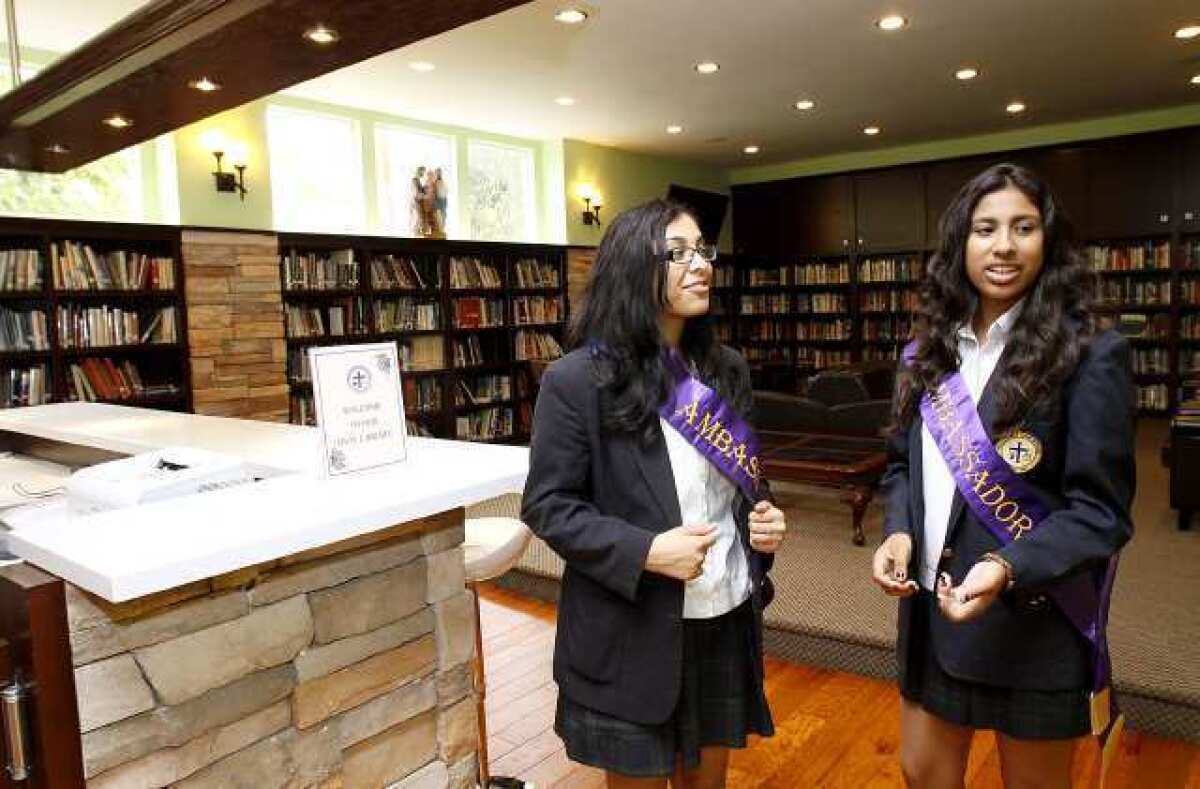 Marisela Avendano, left, and Angelica Rodriguez, right, both juniors, give tour of the facilities, including the school's library, during the Holy Family High School 75th Anniversary Celebration.