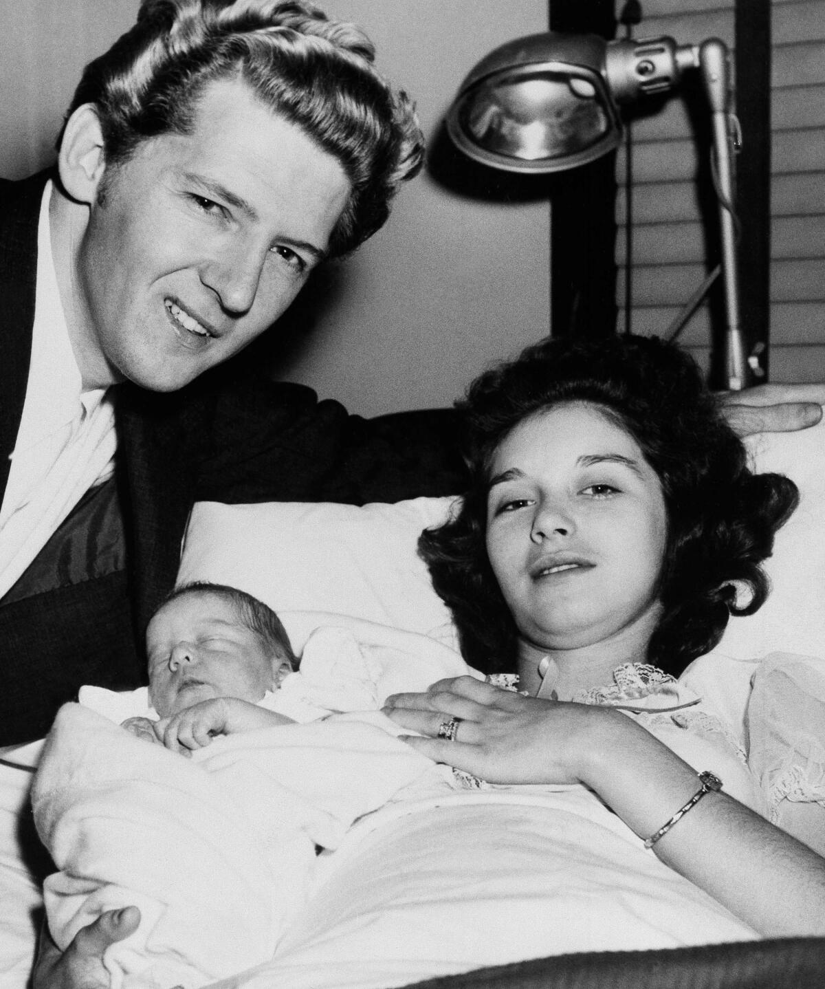 A new father and mother pose for a photo with their newborn baby.