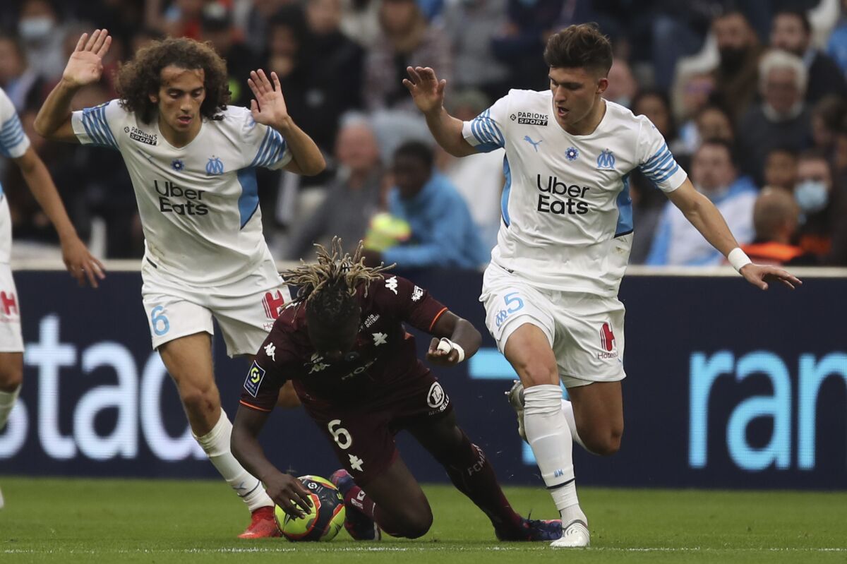 Metz's Kevin N'Doram, center, is challenged by Marseille's Matteo Guendouzi, left, and Marseille's Leonardo Balerdi during the French League One soccer match between Marseille and Metz at the Stade Velodrome stadium in Marseille, Sunday, Nov. 7, 2021. (AP Photo/Daniel Cole)