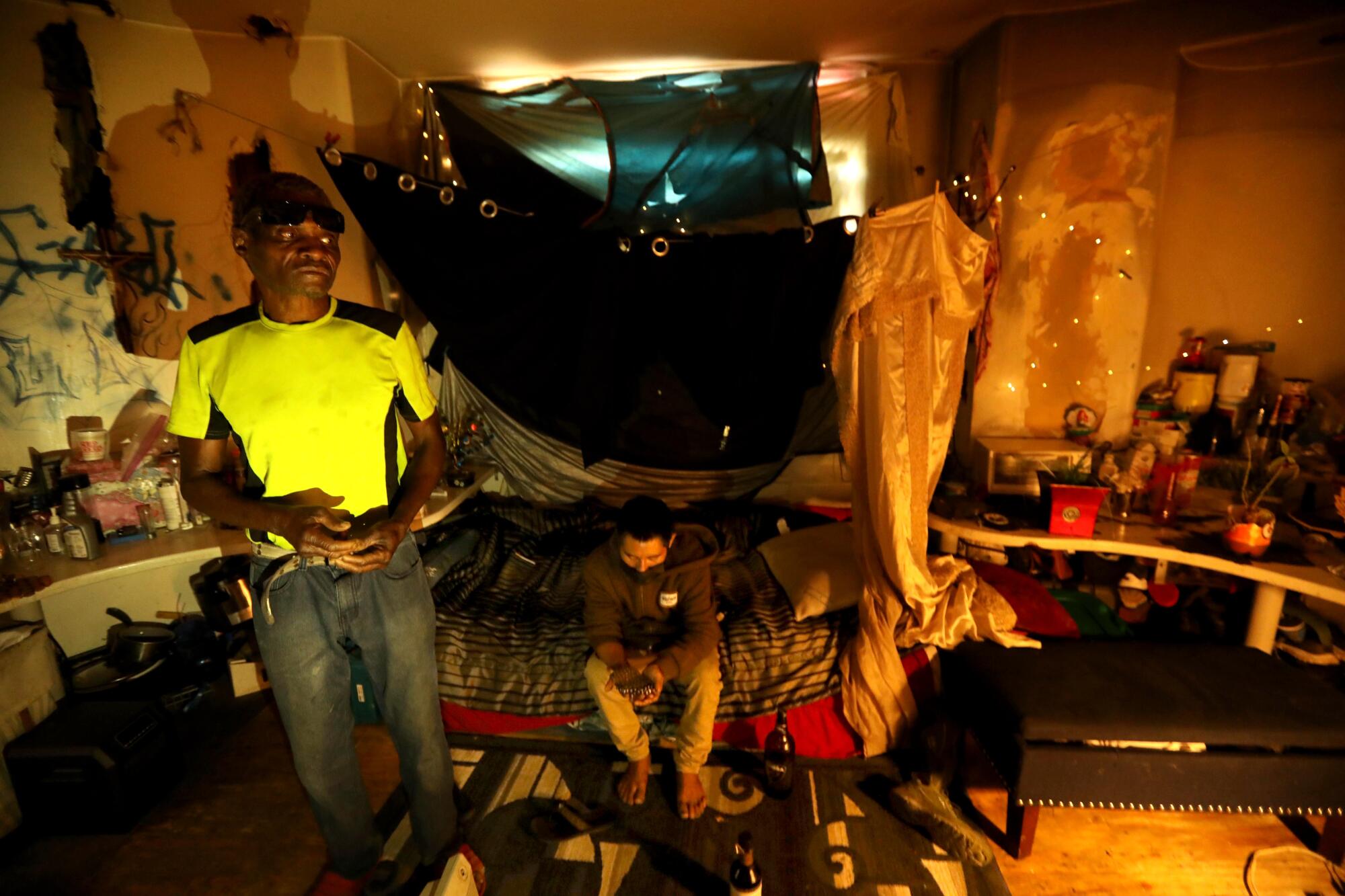 Two men in a room with fairy lights, a twin bed with a canopy and belongings