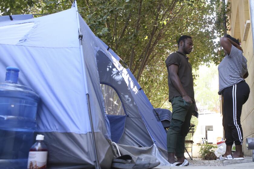 Daniel Ejube, left, and Enjei Grace, from Cameroon, stand next to a tent they have been living in for nearly five months inside a section of a United Nations controlled buffer zone that cuts across ethnically divided Cyprus' capital Nicosia on Wednesday, Oct. 20, 2021. Grace and Ejube have been stuck in a legal limbo inside the buffer zone that separates Cyprus' breakaway north from the internationally recognized south. The U.N. refugee agency says Grace and Ejube should be allowed to apply for asylum in the south. (AP Photo/Philippos Christou)