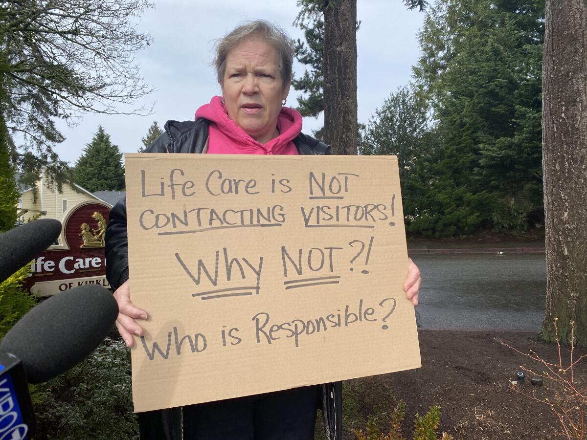 Cheri Chandler, hija de Pat y Bob McCauley, sostiene un letrero el sábado, frente al Life Care Center de Kirkland, criticando al hogar por no advertir a los visitantes que podían haber estado expuestos al coronavirus.