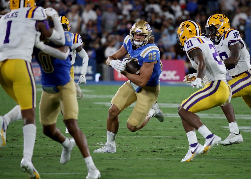 UCLA tight end Greg Dulcich carries a ball while opponents close in on him.