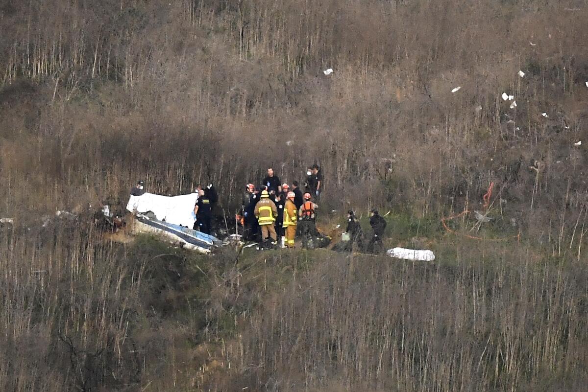 First responders stand near the wreckage of a helicopter in a field.