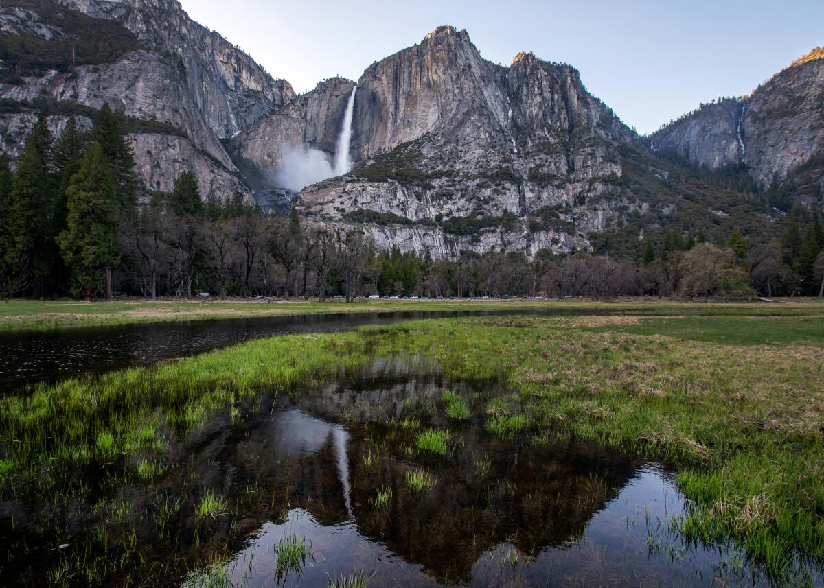 A mountain waterfall is reflected in a meadow.