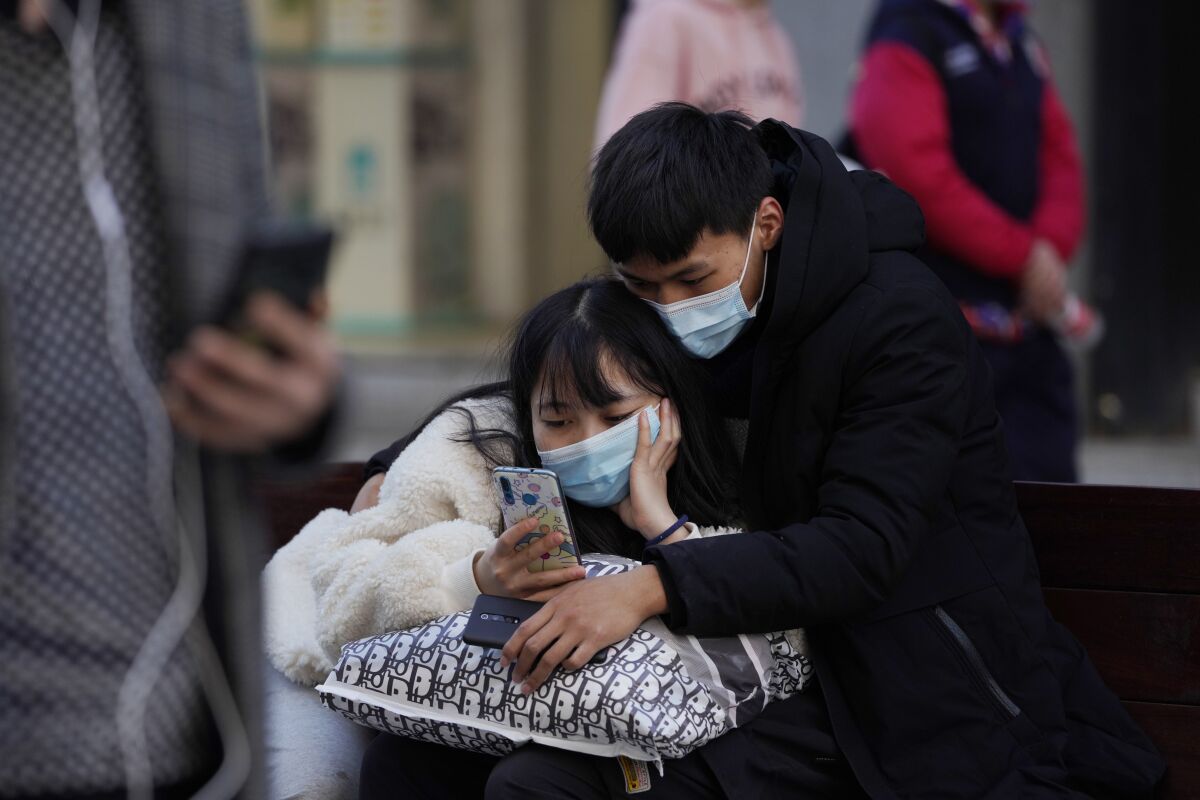 A man and woman wearing masks to help protect themselves from the coronavirus share a smartphone on the street in Wuhan in central China's Hubei province on Thursday, Jan. 14, 2021. A global team of researchers for the World Health Organization arrived Thursday in the Chinese city where the coronavirus pandemic was first detected to conduct a politically sensitive investigation into its origins amid uncertainty about whether Beijing might try to prevent embarrassing discoveries. (AP Photo/Ng Han Guan)