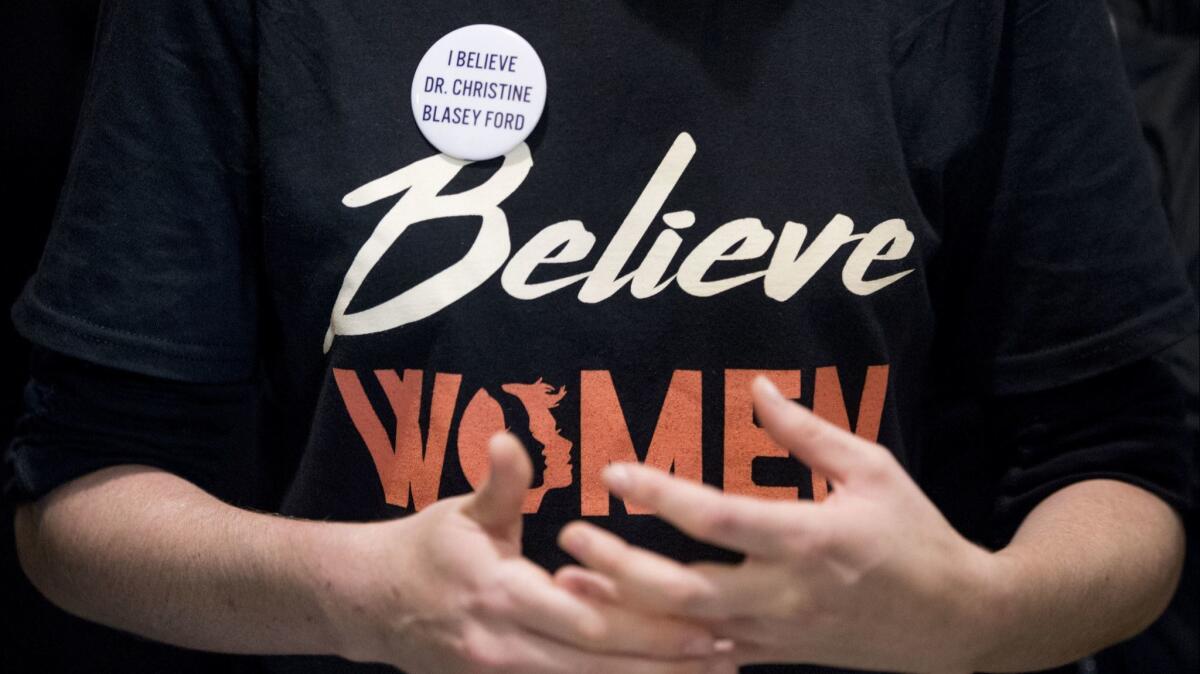 A woman wears a shirt that reads "Believe Women" with a button that reads "I Believe Dr. Christine Blasey Ford."