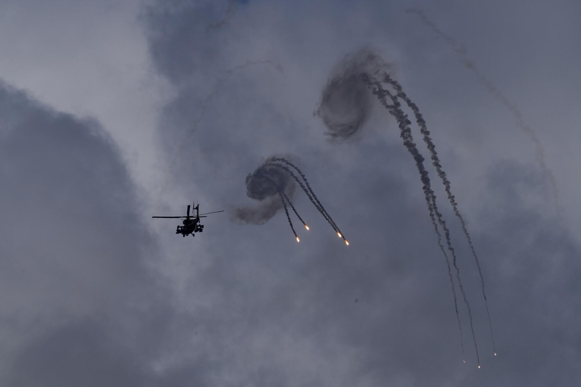 A black helicopter flies near curls of smoke with bright tips in a smoke-filled sky 