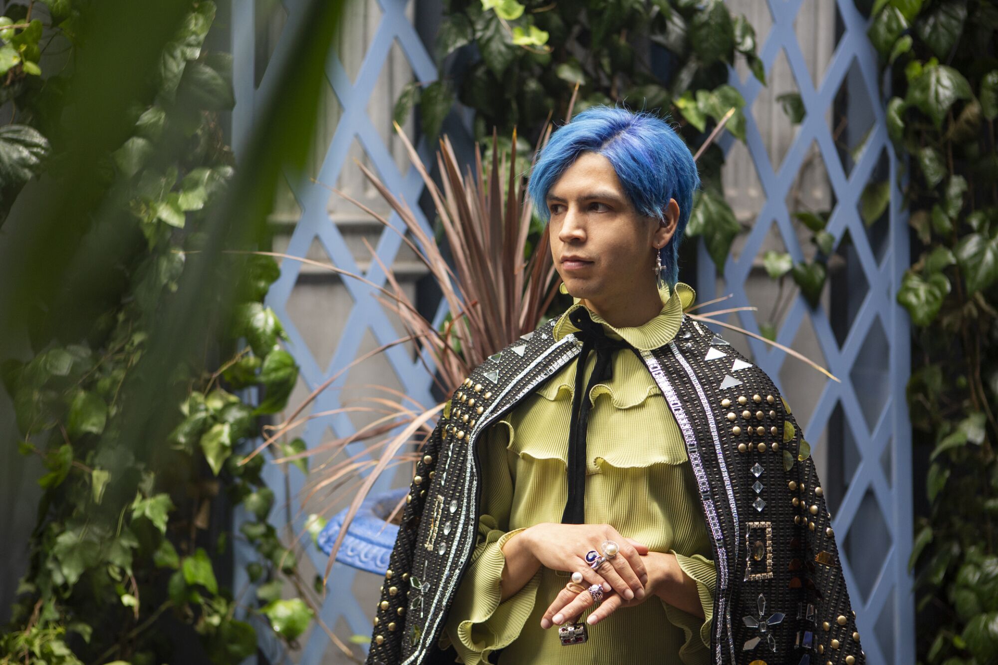 Julio Torres dons bright blue hair and a beaded cape in a scene from Los Espookys.