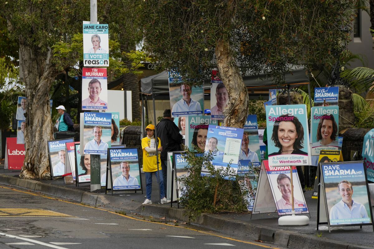A volunteer stands amongst billboards for candidates outside a polling station in Sydney, Australia, Monday, May 9, 2022. Early voting has begun in Australia's federal election with the opposition party hoping the first ballots will reflect its lead over the government in an opinion poll. (AP Photo/Mark Baker)