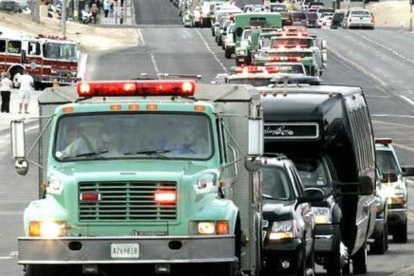 A U.S. Forest Service fire rig carrying the ashes of fallen firefighter Jason McKay leads a long procession of fire protection agency trucks along Hook Blvd. Next of kin follow in the two black vehicles after the funeral at High Desert Church.