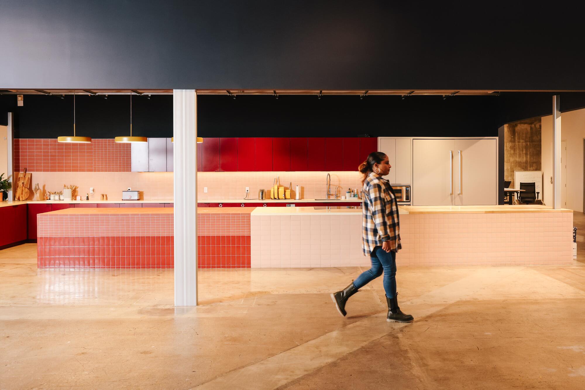 A woman walks past an empty office kitchen.