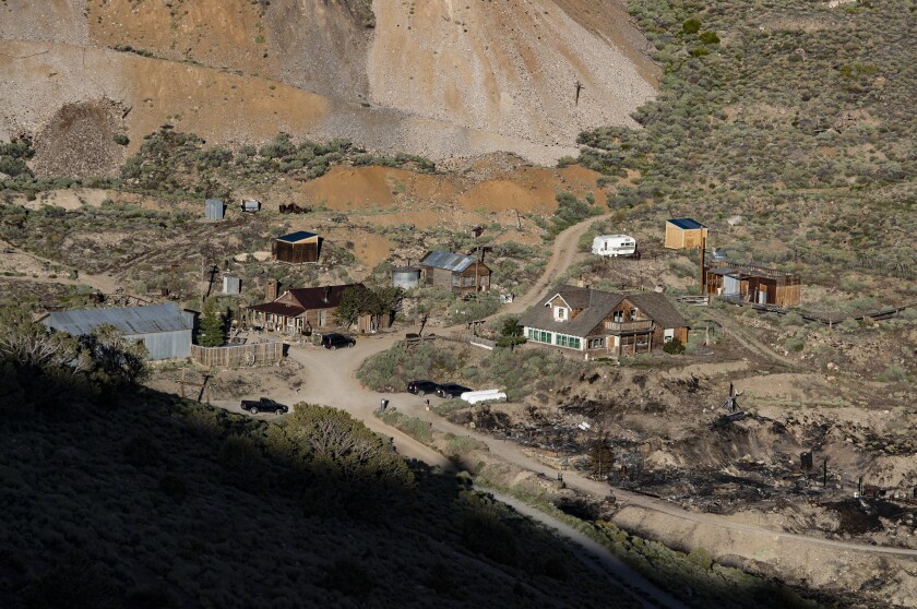 Rustic buildings on a brushy slope below mine tailings near the blackened ground where Cerro Gordo's American Hotel burned.