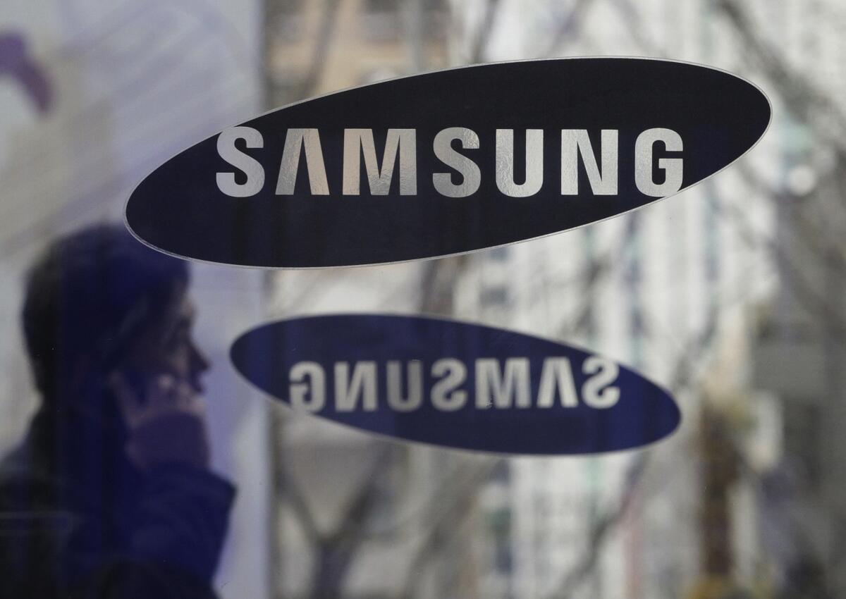 A man with a mobile phone walks by Samsung Electronics logos at the compnay's headquarters in Seoul on Dec. 12, 2013.