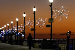 Huntington Beach, CA - December 12: 80 snowflakes light up the Huntington Beach Pier as pier walkers are silhouetted by the sunset's glow amid pleasant weather in Huntington Beach Tuesday, Dec. 12, 2023. (Allen J. Schaben / Los Angeles Times)