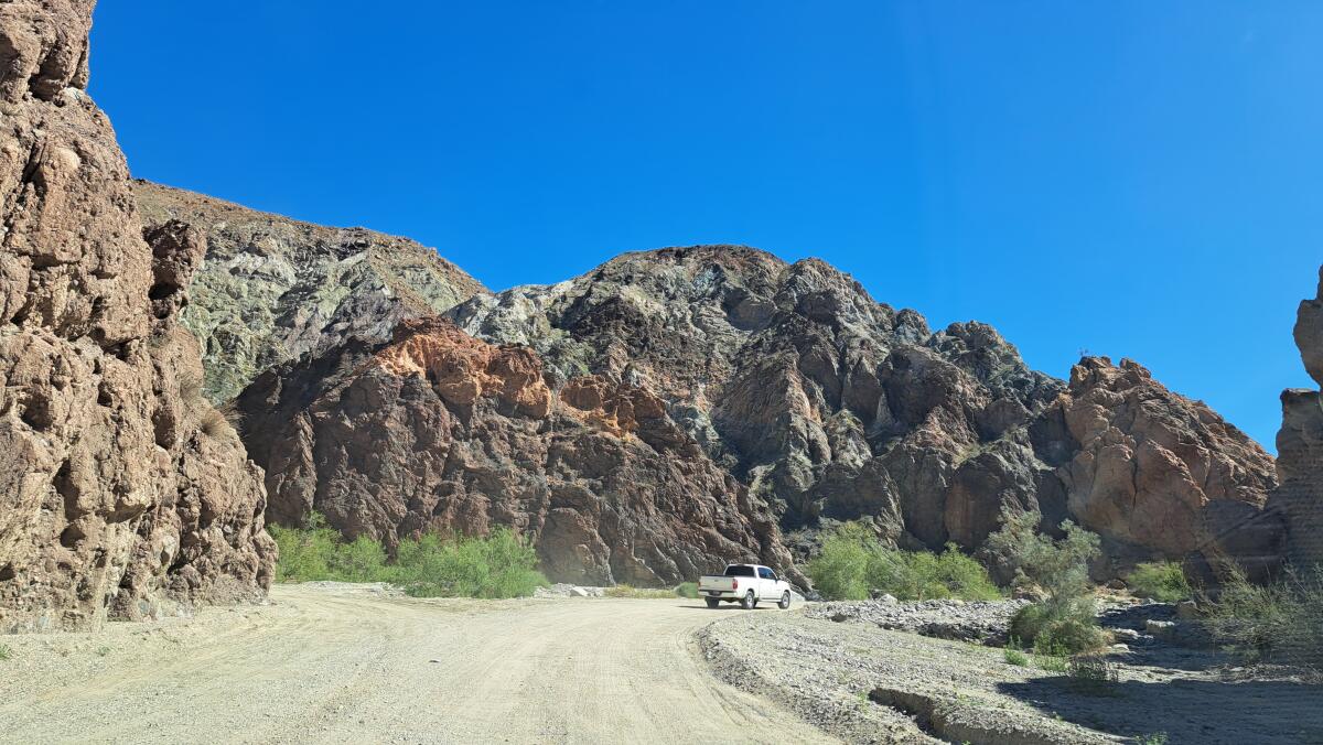 A pickup truck drives along a dirt road in a canyon.
