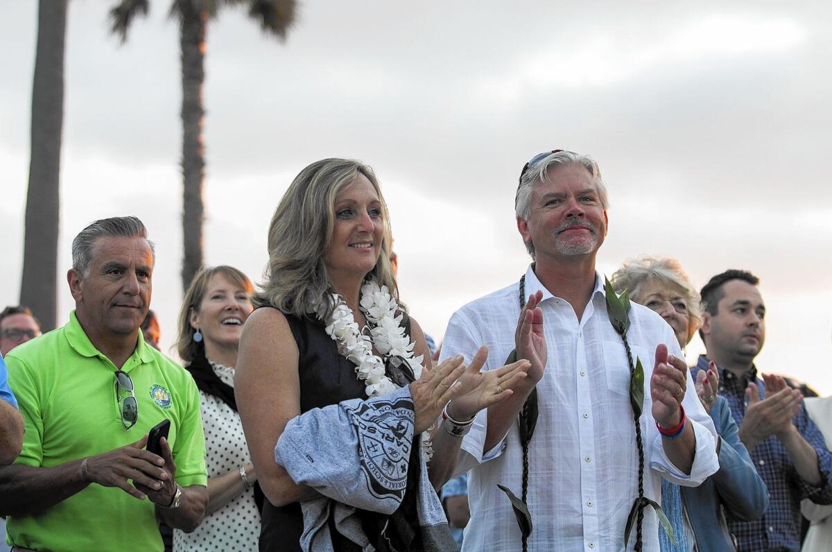 Teri and Chris Carlson, the parents of Ben Carlson, applaud during Wednesday's unveiling of the stainless-steel likeness of their late son Ben at McFadden Square in Newport Beach.