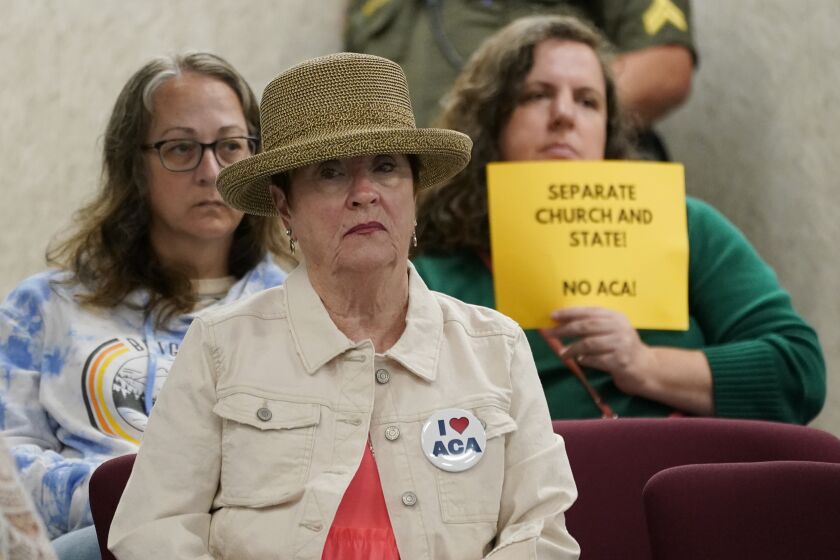 FILE - A woman wearing a button supporting charter schools linked to Hillsdale College sits in front of a woman holding a sign opposing the schools during a meeting of the Tennessee Public Charter School Commission staff on Sept. 14, 2022, in Murfreesboro, Tenn. A contentious charter school operator linked to a conservative Michigan college is taking another swing at opening schools in three Tennessee counties that have previously rejected it, as well as in two new counties. (AP Photo/Mark Humphrey, File)