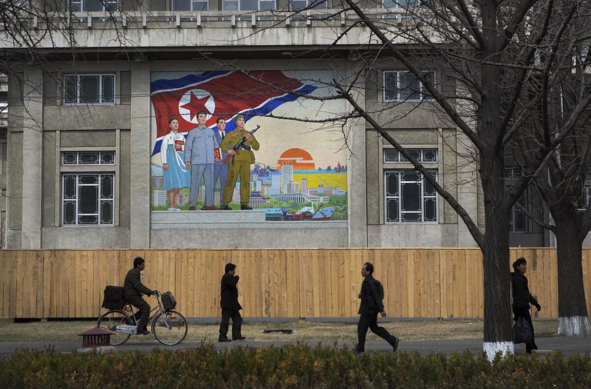 North Koreans pass by a large nationalist painting in Pyongyang.
