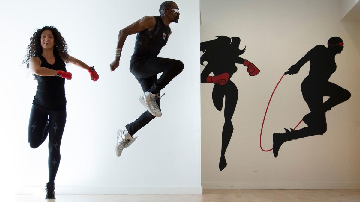Leila Fazel and Olajide mimic murals on the wall at their new gym.
