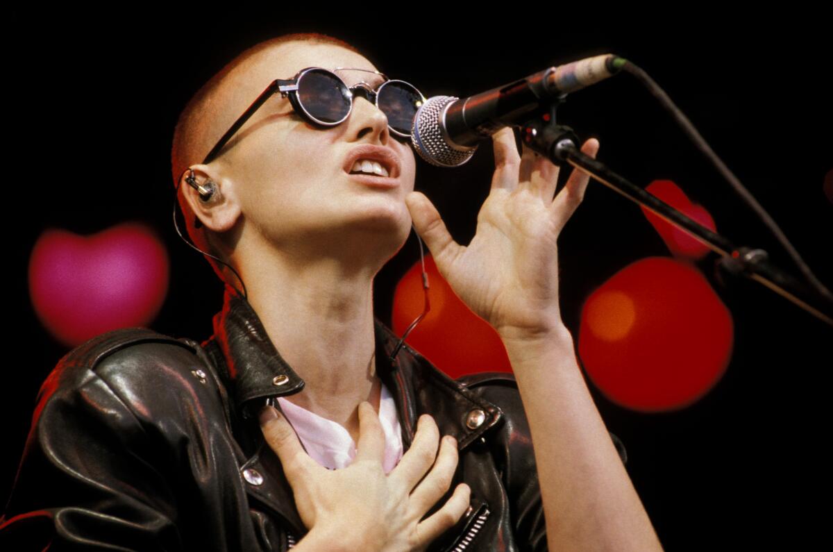 Sinead O’Connor in dark sunglasses singing into a microphone in 1990