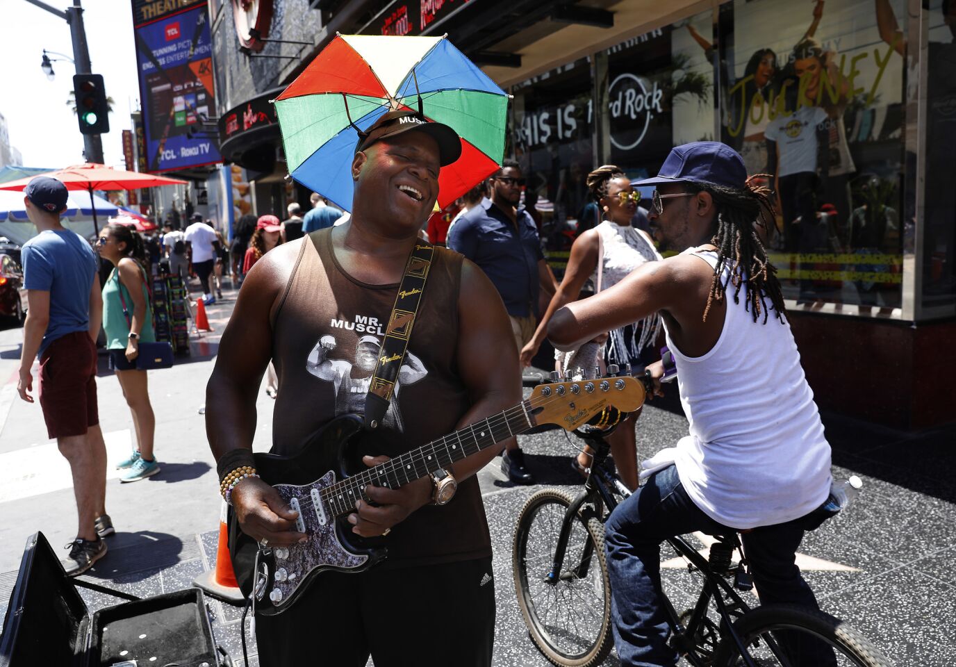 A performer known as Dr. Funkstein shields himself from the sun while playing his guitar near Hollywood Boulevard and Highland Avenue.
