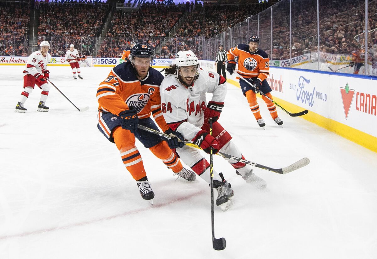 Carolina Hurricanes' Jalen Chatfield (64) and Edmonton Oilers' Connor McDavid (97) vie for the puck during the second period of an NHL hockey game Saturday, Dec. 11, 2021, in Edmonton, Alberta. (Jason Franson/The Canadian Press via AP)