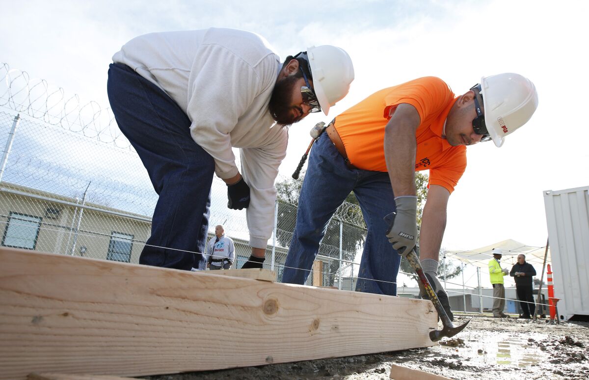 Two young men in hard hats work with lumber on construction site