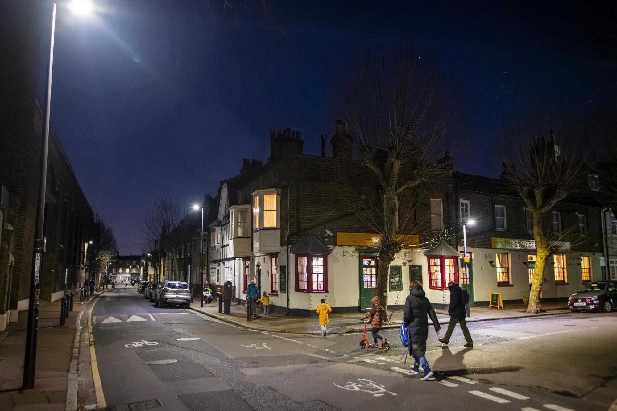 Street scene of a lighted-up pub with people walking by at night 