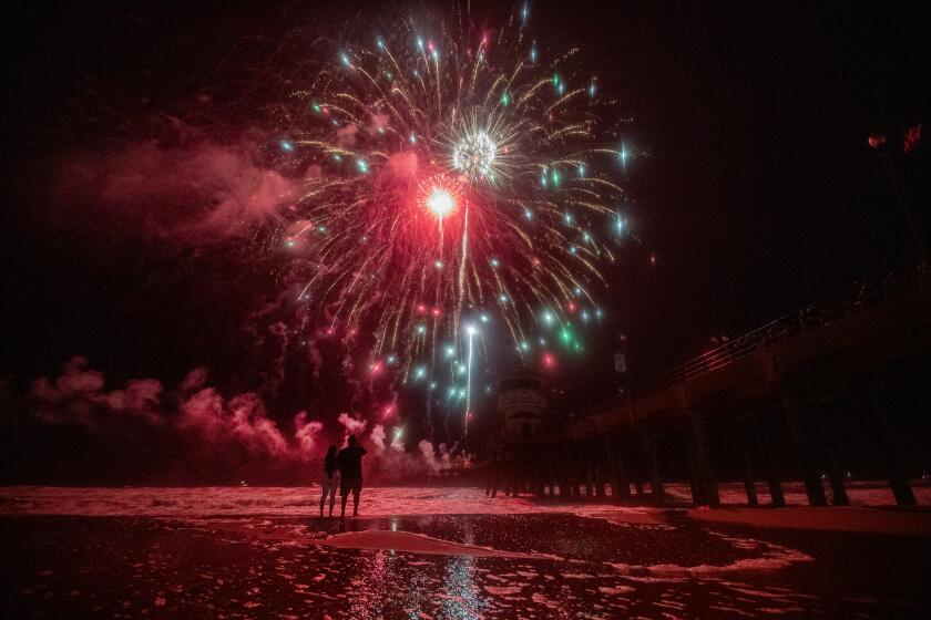 Huntington Beach, CA - July 04: A couple wade into the high tide surge to get a closer look at the fireworks celebration over the ocean at the pier in Huntington Beach Tuesday, July 4, 2023. (Allen J. Schaben / Los Angeles Times)