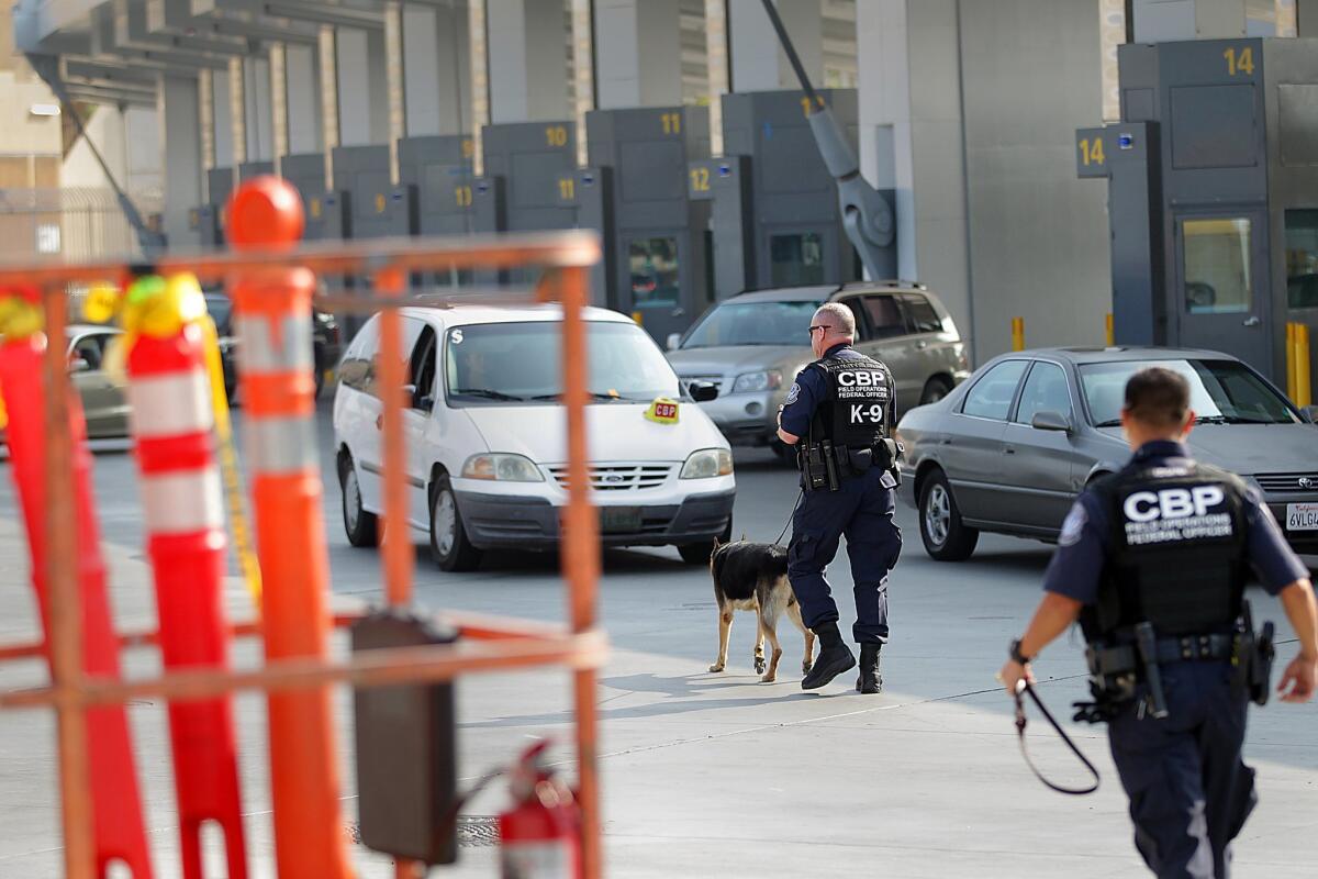 Customs and Border Protection officers, one with a K-9, walk near inspection lanes recently opened at the San Ysidro Port of Entry.