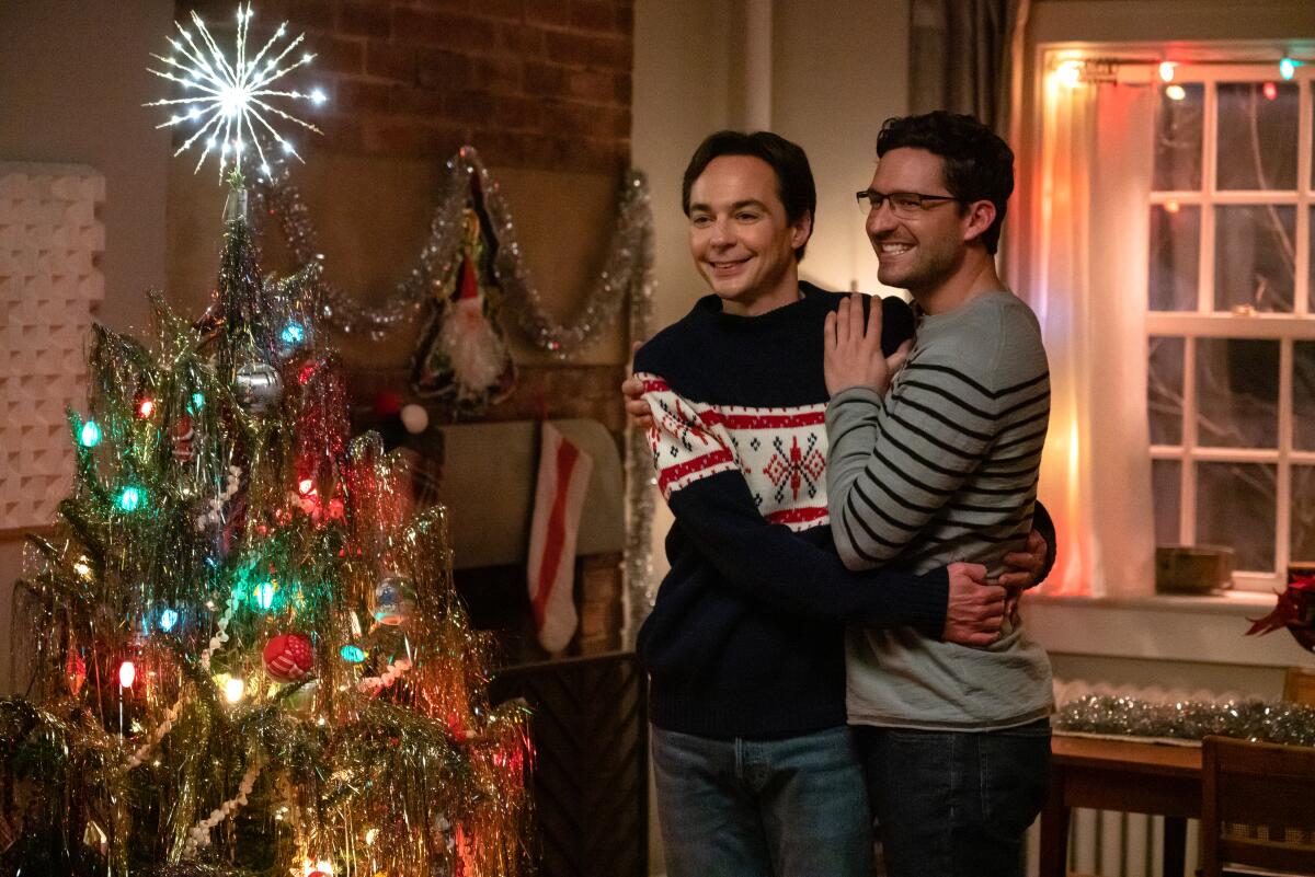 A male couple hug as they stand beside a lighted Christmas tree.