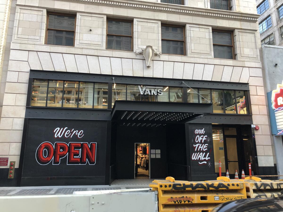 A Beaux Arts building houses a Vans store with painted black plywood that advertises "We're Open."
