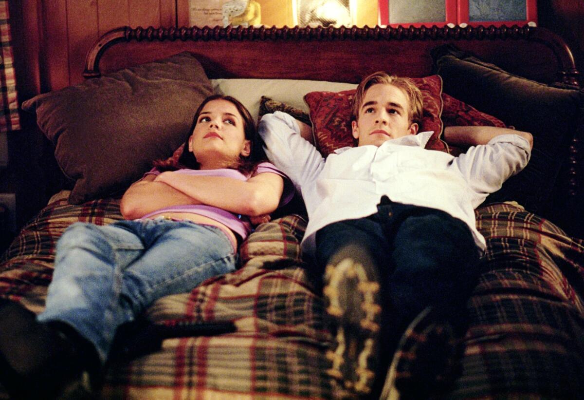A teenage boy and a teenage girl wearing clothes lie on a bed.
