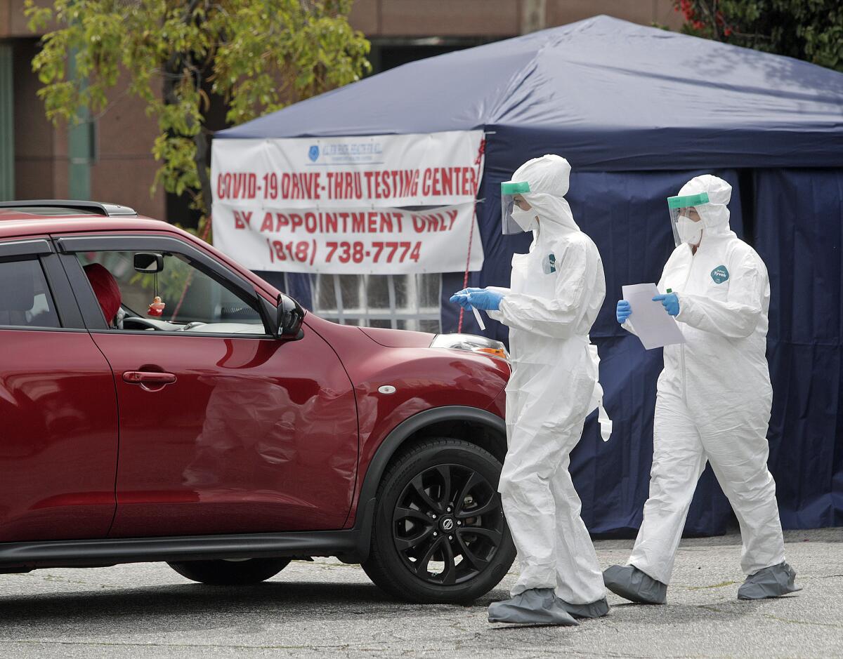 Two health workers advance to a vehicle with people inside who wanted to be tested for the coronavirus at a drive-through testing station installed by All For Health, Health For All on the corner of Isabel Street and Broadway in Glendale on Tuesday.