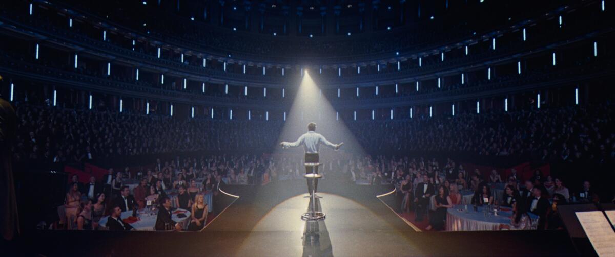 A man stands in the spotlight on a stage, looking out at the audience.