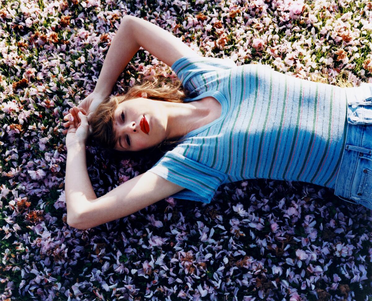 Taylor Swift lies on rocky ground, her arms above her head.