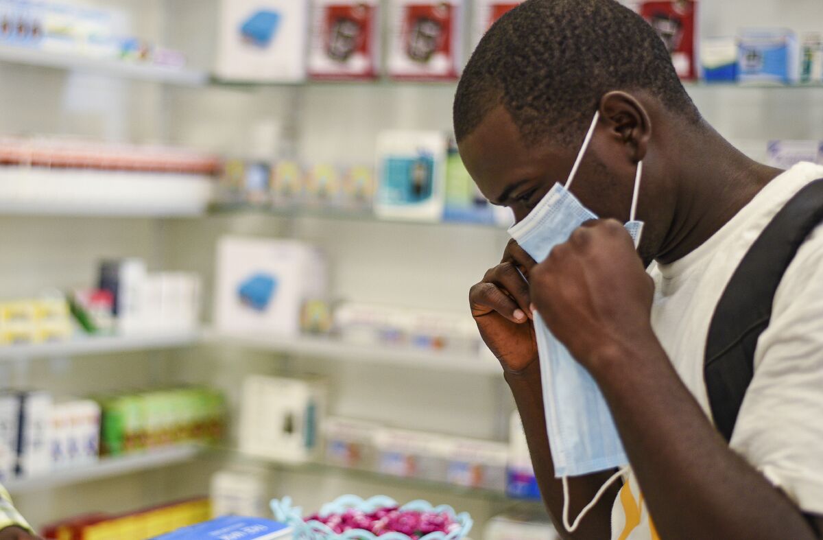 FILE — In this Feb. 6, 2020, file photo, a man tries on a face mask at a pharmacy in Kitwe, Zambia. Facing financial difficulties aggravated by the coronavirus pandemic, the southern African nation of Zambia seems to be headed for a default on debt owed to private investors. (AP Photo/Emmanuel Mwiche, File)