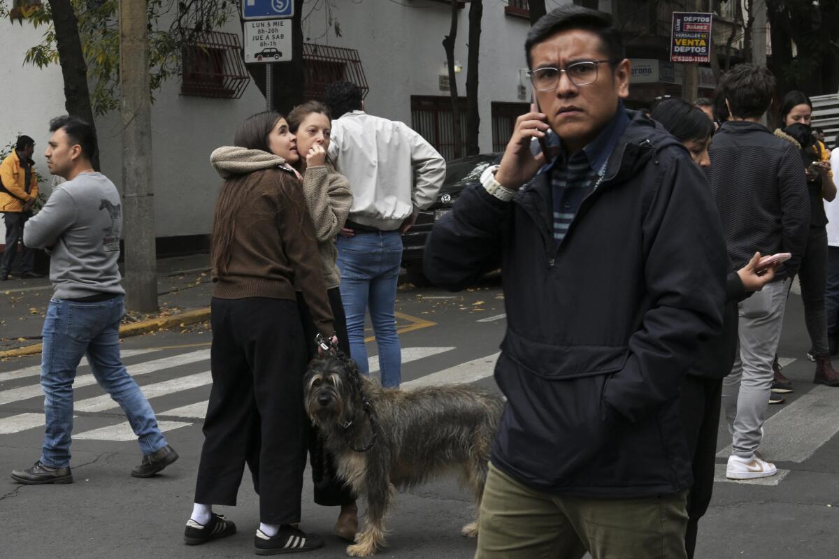 A man talks on a cellphone near other people and a dog standing on a street