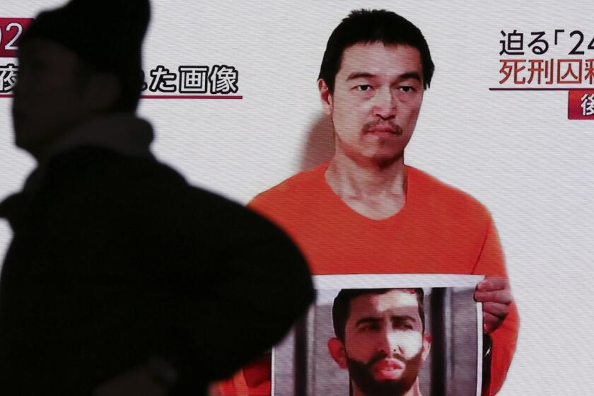 Japanese hostage Kenji Goto holds what appears to be a photo of Jordanian pilot Lt. Moaz Kasasbeh in a YouTube video projected on a big screen TV on Wednesday. The Islamic State hostage has reportedly been beheaded by his captors.