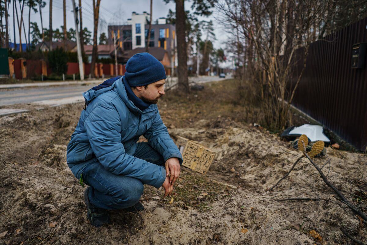A man squats next to a road, lost in thought, near a body covered with a cloth