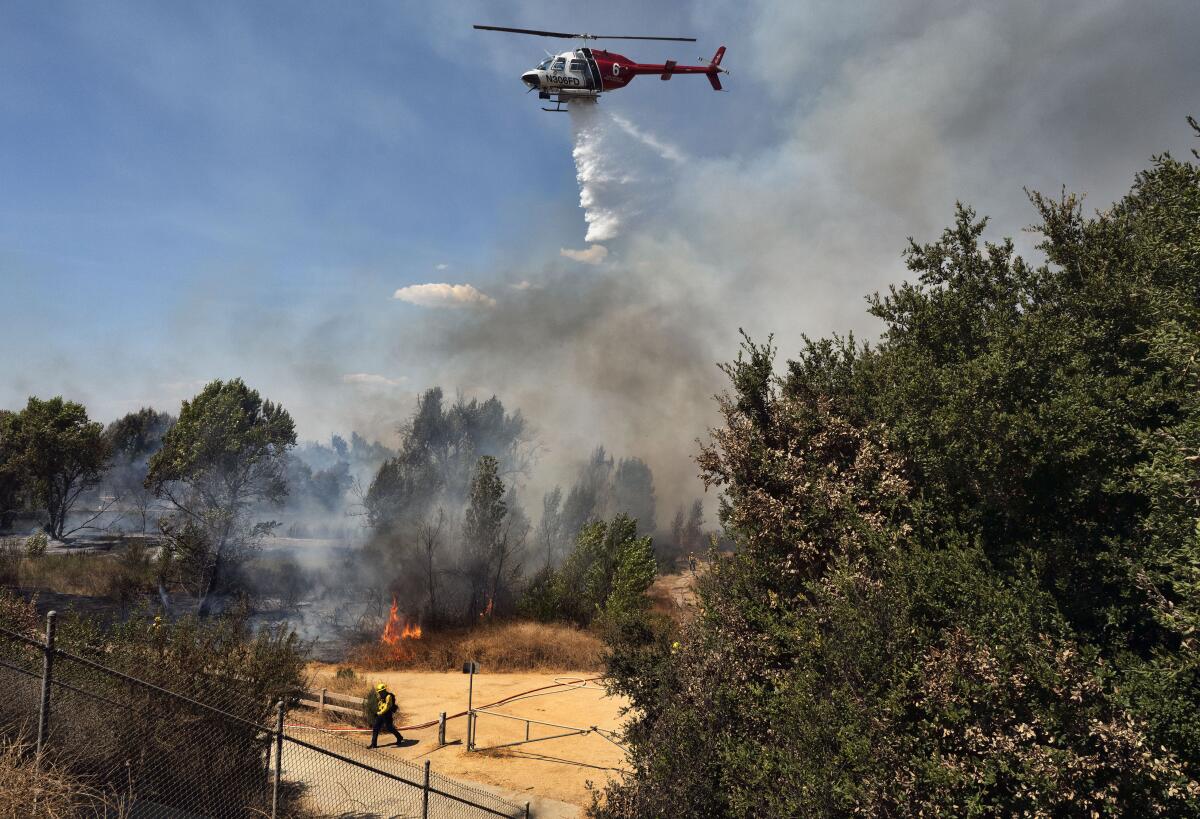Un helicóptero del Departamento de Bomberos de Los Ángeles arroja agua sobre maleza ardiendo 