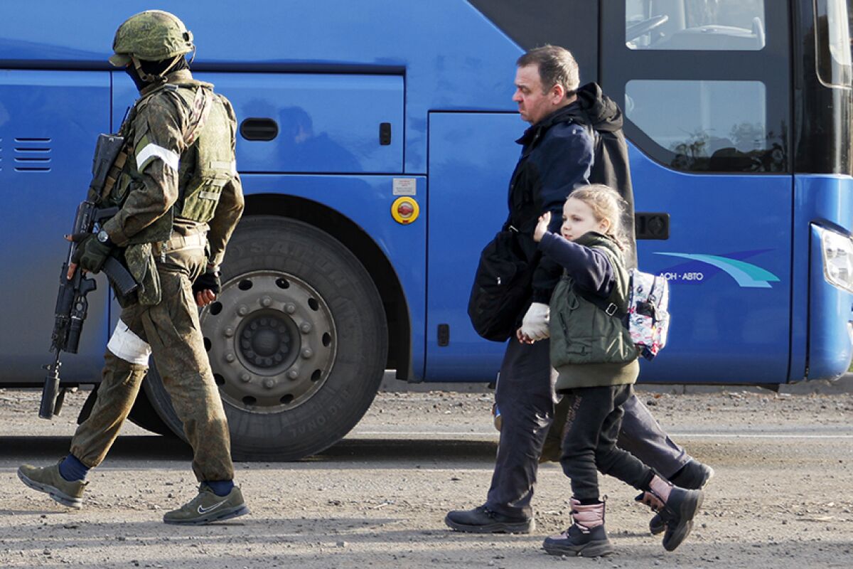 A man and a child are escorted to a bus by a soldier.