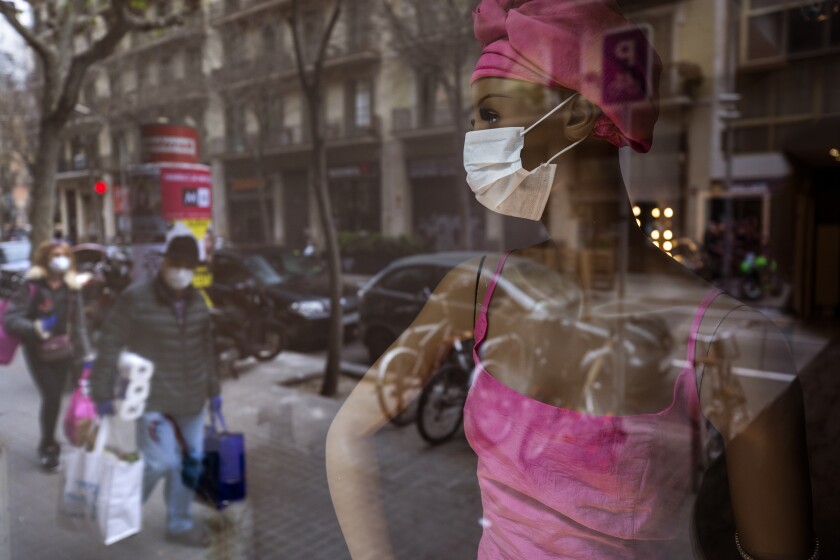 People wearing masks and carrying supplies walk past a mannequin wearing a mask in Barcelona, Spain.